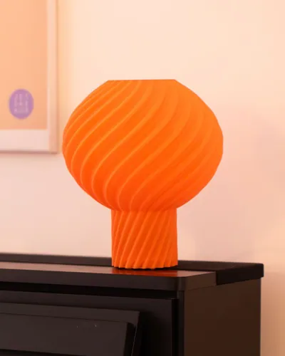 Oranje Helio Lamp met gedraaide lampenkap op een donker dressoir